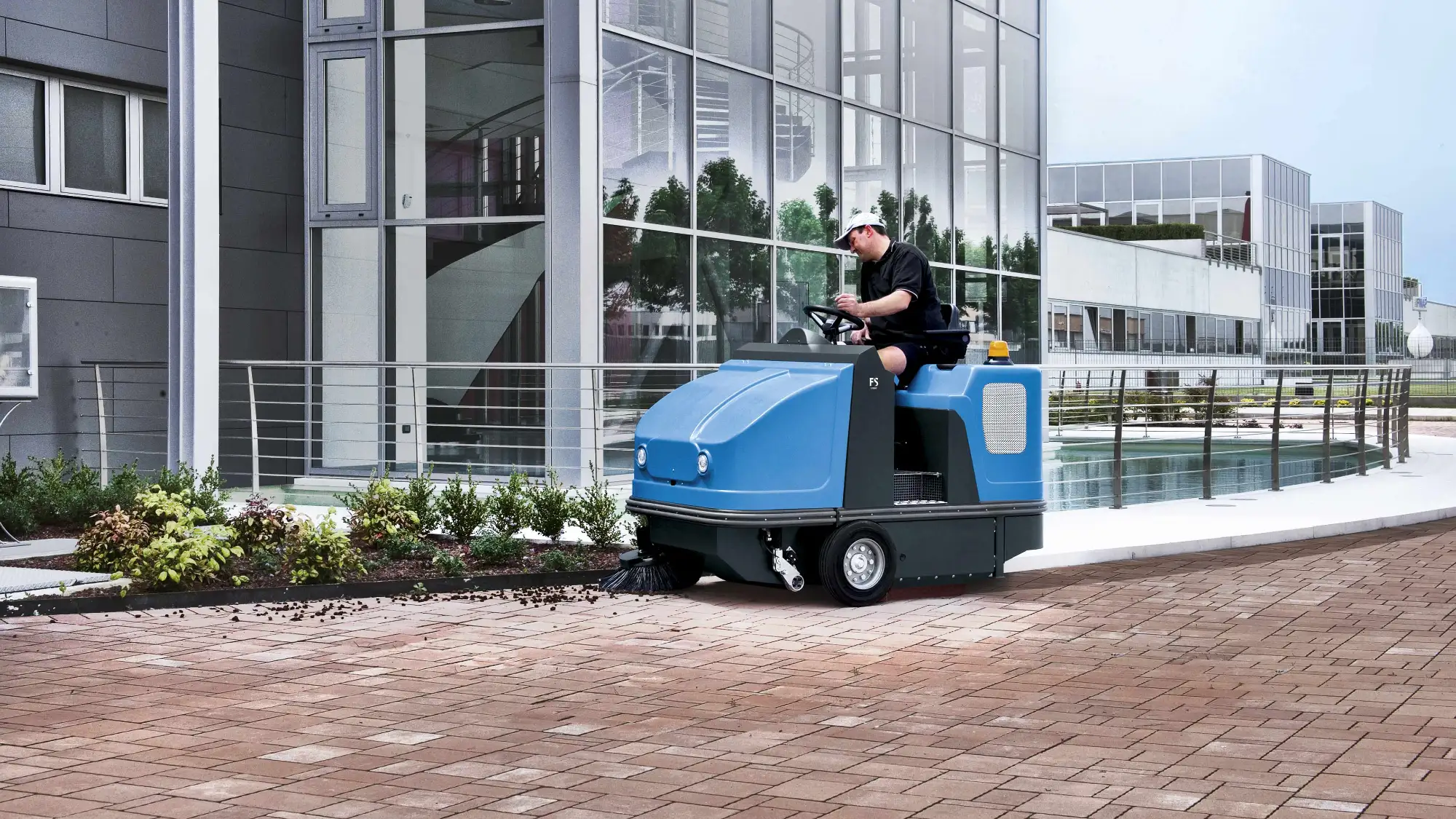 Fimap ride-on sweeper clearing debris from pavers outside an office building